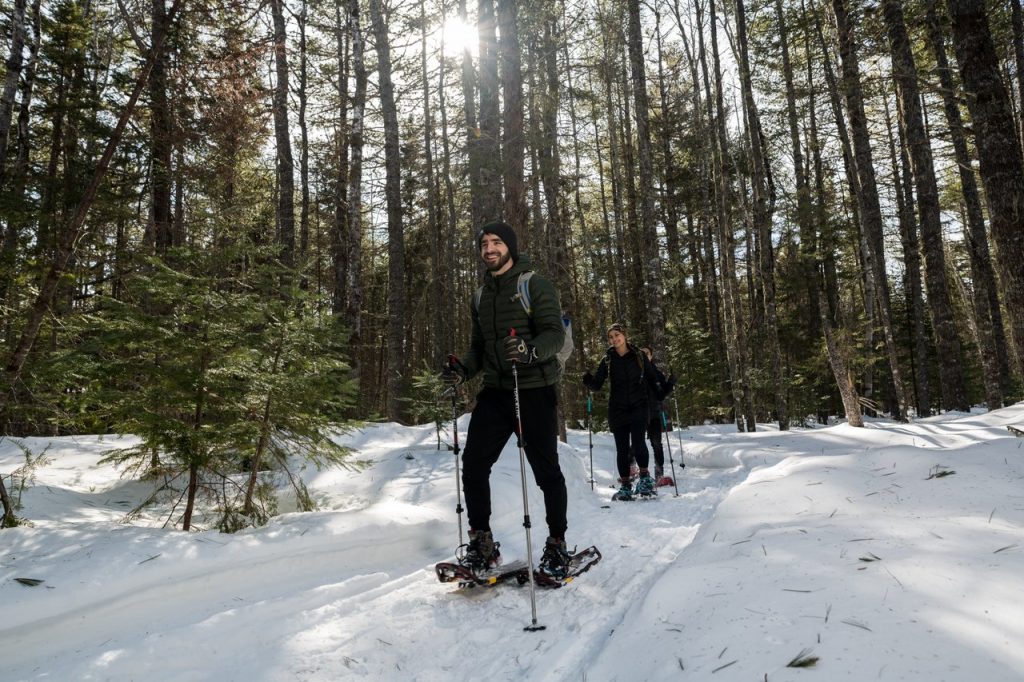 A vibrant winter sports scene at Sugarloaf Provincial Park New Brunswick showcasing a skier and a family enjoying skiing along with a distant view of a ski lift.