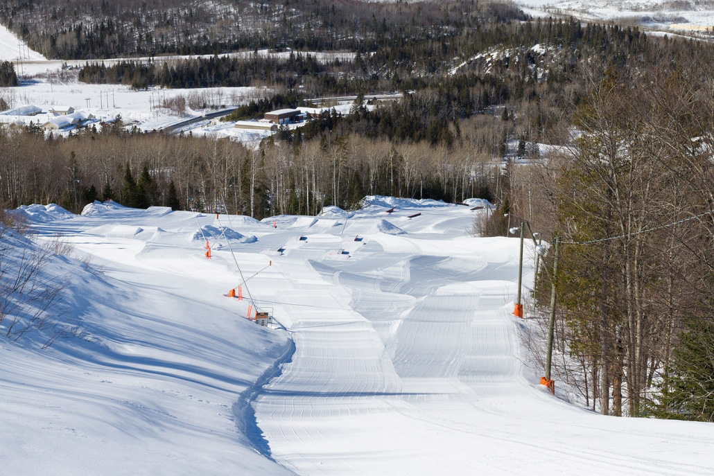 Winter scene at Sugarloaf Provincial Park in Atholville, New Brunswick, Canada showcasing a bustling ski resort. The landscape is dotted with skiers enjoying the snow-covered slopes.