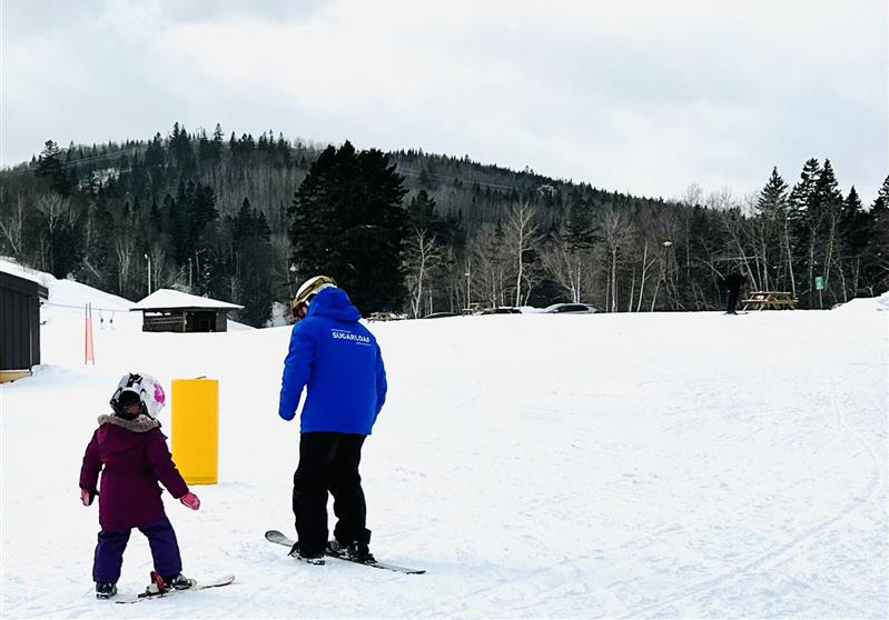 Winter sports scene at Sugarloaf Provincial Park, New Brunswick, showing a challet, winter sports centre, and a family skiing at the ski resort.