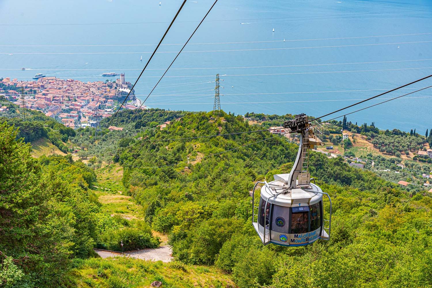 Prà Alpesina Chairlift - Upper terminal in Italy - a cable car going up a hill with the city in the background.