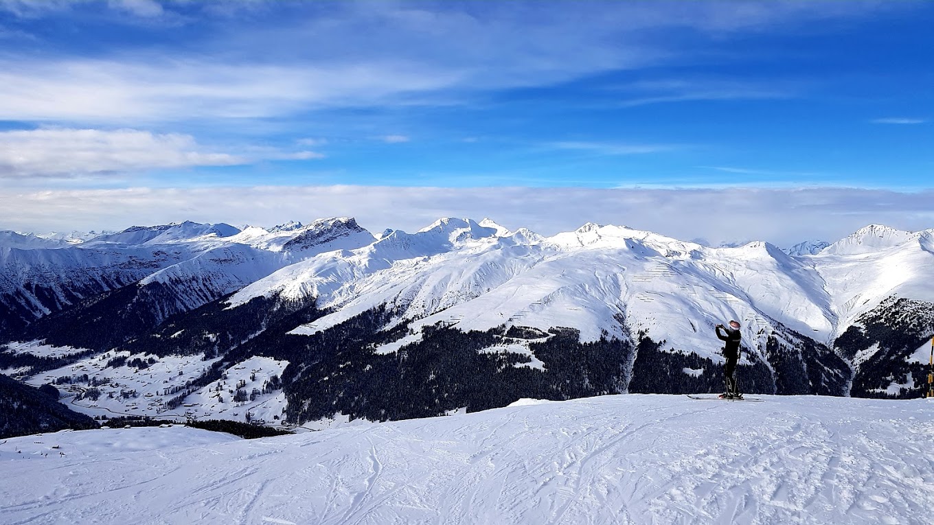 View of Jakobshorn ski resort in Eastern Switzerland featuring a chalet nestled in snow-covered slopes, buzzing with winter sports activities against the backdrop of a majestic mountain.