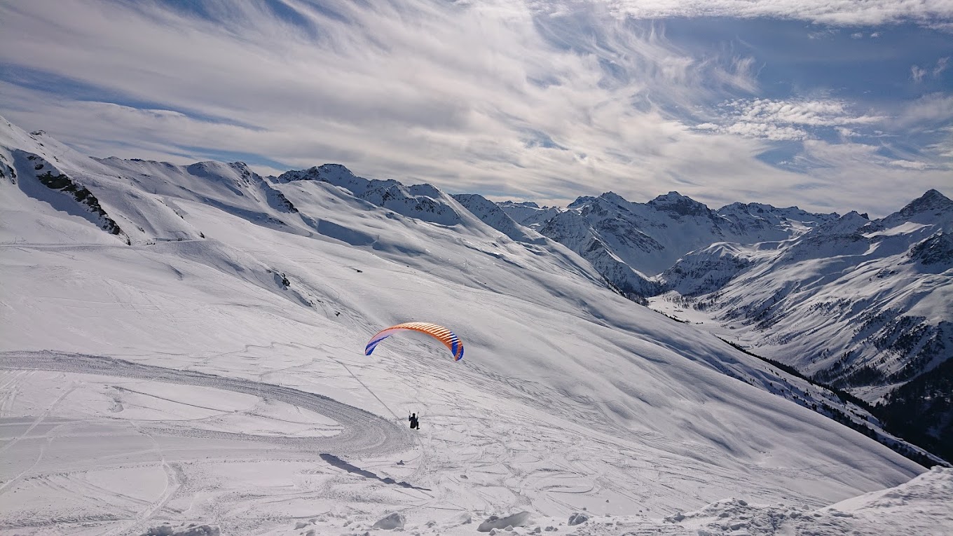 A skier navigates a scenic winter landscape at the Jakobshorn ski resort in Graubünden Eastern Switzerland. Snow-covered peaks encase a cozy welcoming chalet in the background.