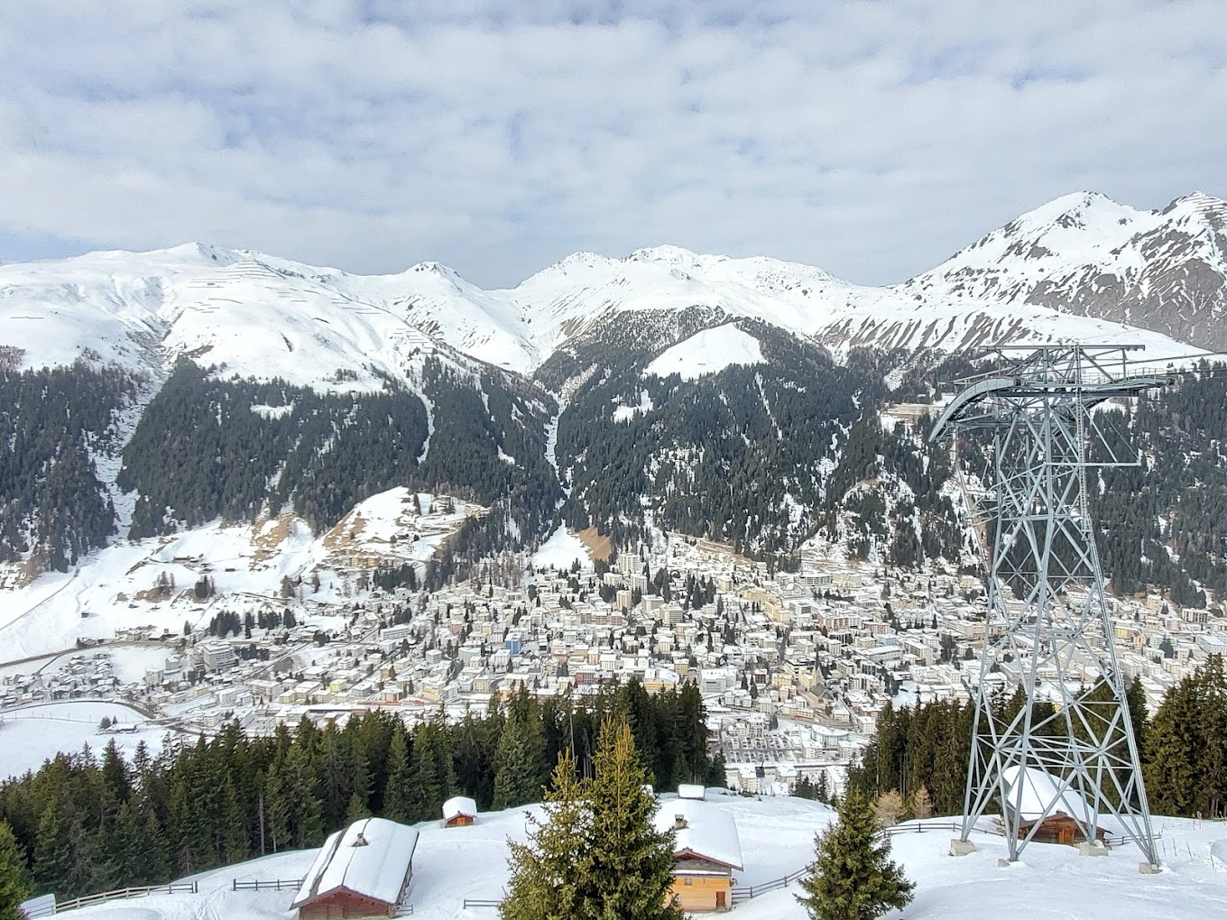 View of the picturesque Jakobshorn ski resort in Graubünden, Switzerland, featuring a charming chalet, ski slopes blanketed in snow, and a ski lift carrying enthusiasts to their winter sports activities.
