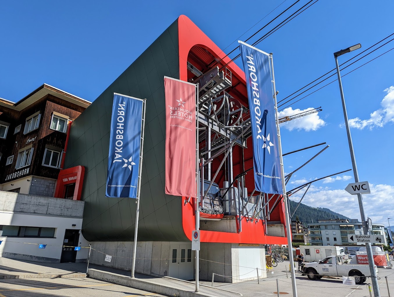 Sunny view of Jakobshorn in Switzerland showcasing a charming chalet and a winter sports center, with a ski lift and resort subtly visible against the stunning snow-covered backdrop.