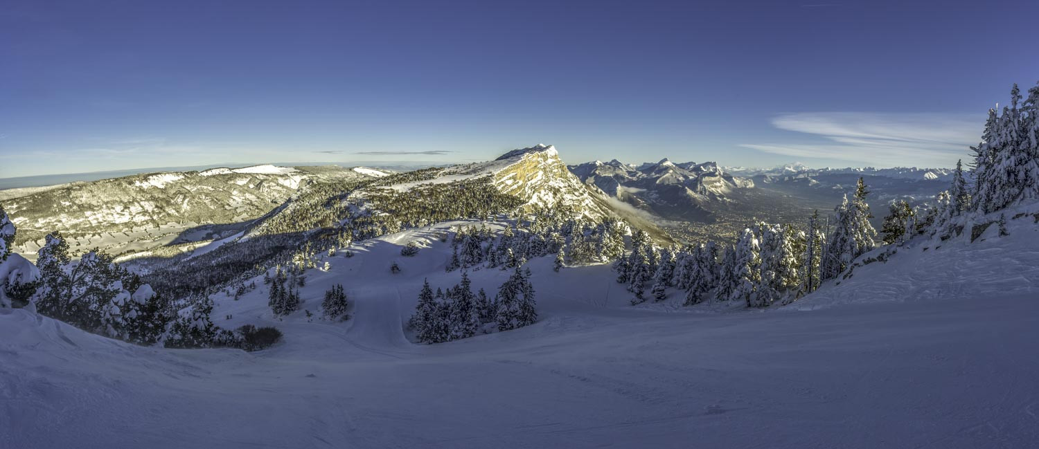Scenic winter view of Lans en Vercors in France featuring a lively ski resort snow-covered slopes and majestic mountains in the backdrop. A bustling winter sports scene adds energy to the serene setting.