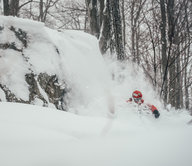 A skier is enjoying a winter sports scene at Mont Gleason in Tingwick, Quebec, Canada, with hints of a snowboarder and snowmobile in the background, nearby a small challet.