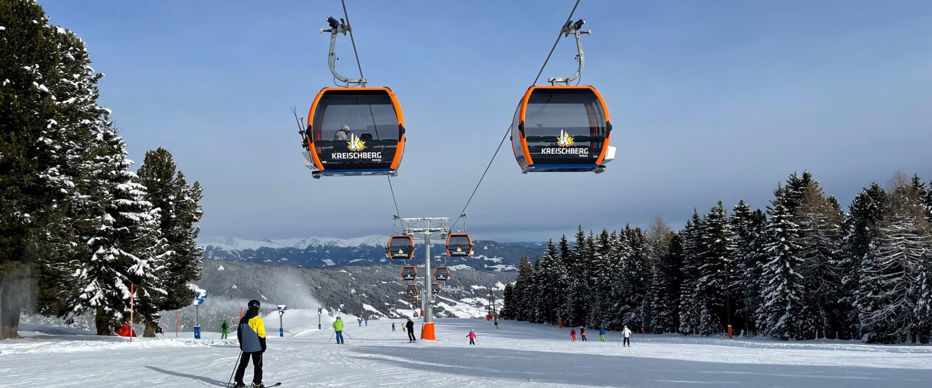 A lively scene at the Kreischberg ski resort in Styria Austria featuring a ski lift carrying skiers up the snow-covered mountain with a cozy chalet in the background.