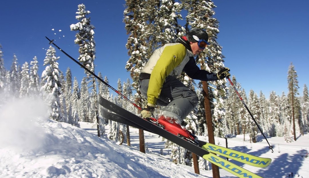 A skier and a snowboarder enjoy the snowy slopes at Badger Pass, Yosemite National Park. A ski lift can be seen in the back, indicating this is part of a ski resort.