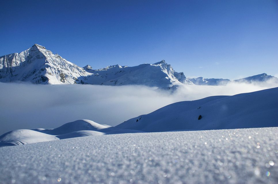 Spectacular winter scene at Tschappina ski resort, Switzerland, featuring a skier zipping downhill, surrounded by pristine snow. A cozy chalet nestles nearby adding charm to the stunning scenery.