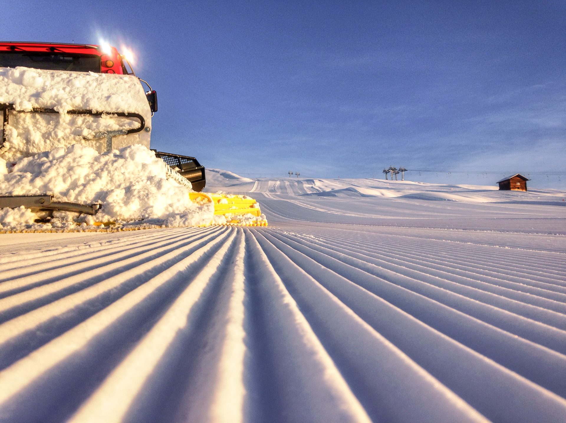 Winter scene at the Tschappina-Lüsch-Urmein ski resort in Eastern Switzerland, featuring snow-covered slopes, skiers, a snowmobile, and a ski lift in action.