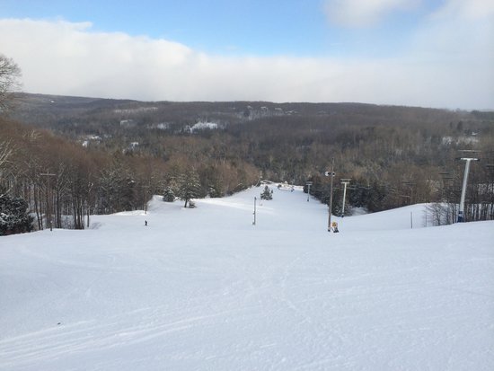 A picturesque winter scene in Otsego Gaylord Michigan showcasing a bustling ski resort. The image captures snow-covered slopes skiers ascending through a ski lift and a cozy challet nestled nearby.