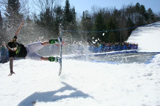 A lively winter sports scene in Gaylord Michigan USA shows a skier gliding down a snow-covered slope. A bustling winter sports centre possibly a challet is visible in the backdrop creating a vibrant winter atmosphere.
