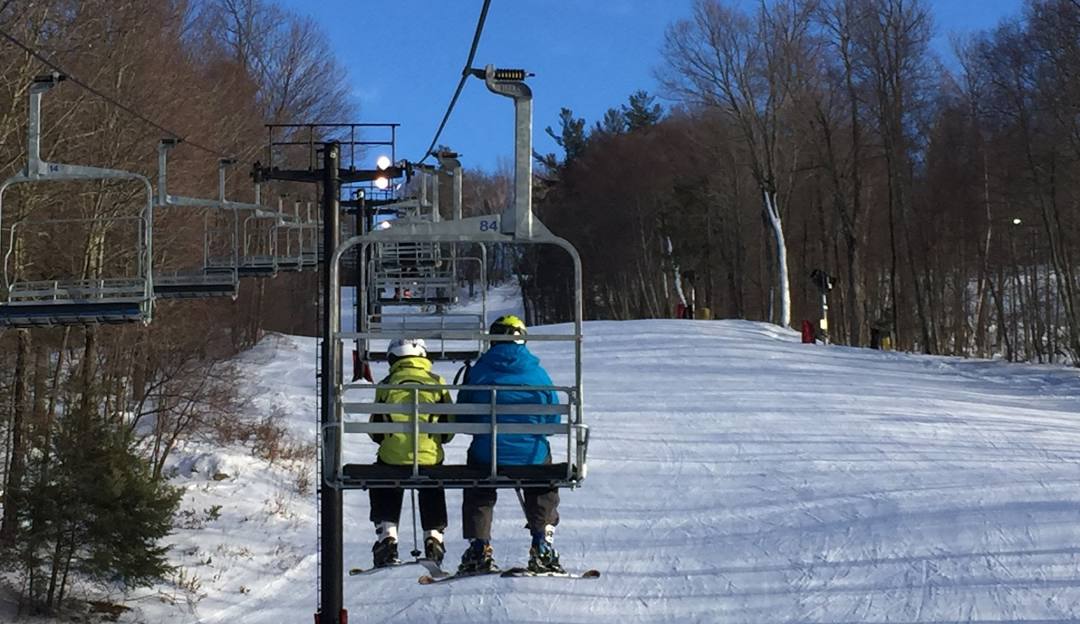 A vibrant winter scene at Mohawk Mountain Ski Resort in Cornwall Connecticut featuring a ski lift and skiers enjoying the snowy slopes. Some appear to be a family skiing together.