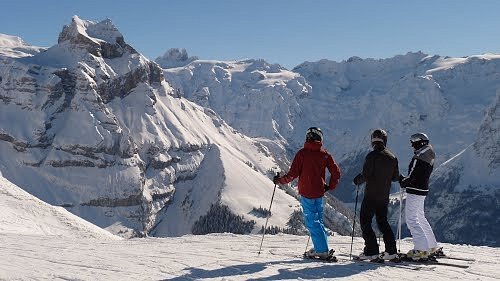 Winter scene at Brunni-Bahnen ski resort in Engelberg, Switzerland featuring a challet, some skiers, and family enjoying skiing.