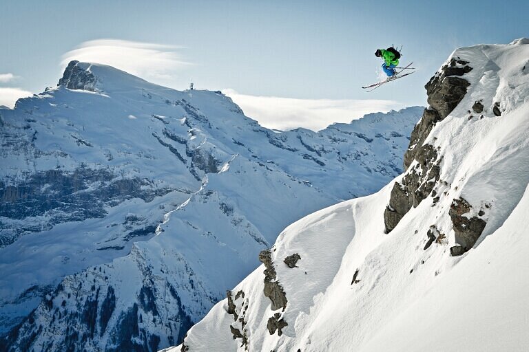 A snowboarder carving through the pristine slopes at Brunni-Bahnen Engelberg-Titlis against the breathtaking backdrop of the Swiss Alps under a clear blue sky.