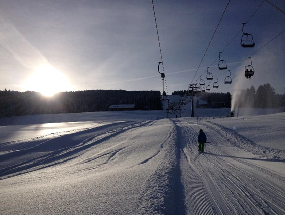 A skier enjoys the winter sports scene at Grüntenlifte – Kranzegg in Bavaria, Germany. A charming chalet and ski lift can be seen nearby, enhancing the picturesque ski resort setting.