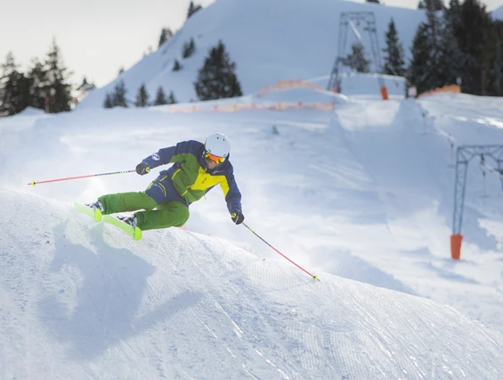 A skier glides down the slopes of Grüntenlifte – Kranzegg ski resort in Bavaria, Germany, with a snowboarder and a chalet in the background on a wintry day.