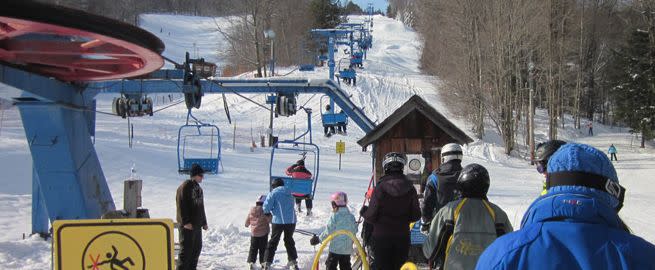 Winter scene at a ski resort in Buffalo, Greater Niagara, with ski lifts running though mountains covered in snow. Families enjoying winter sports at the snow-covered base.