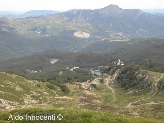 View of a charming chalet nestled at Cerreto Laghi Monte La Nuda, a serene ski resort in Italy. A mountain bike is visible near the chalet and a scenic mountain range provides a breathtaking backdrop.