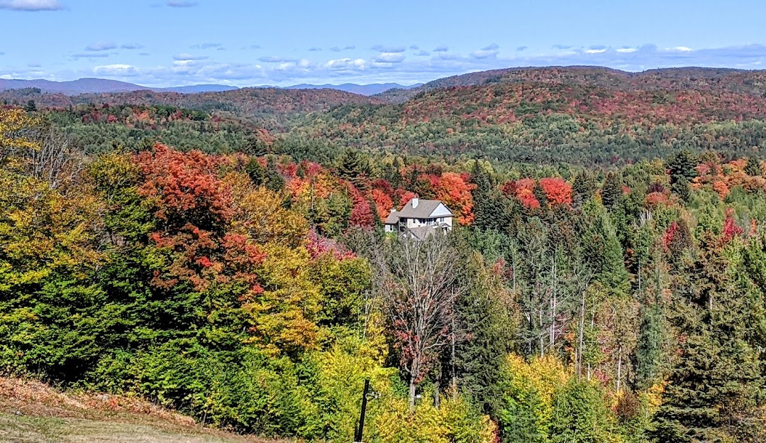 A scenic view of Montcalm in Lanaudière, Rawdon, Quebec, with a charming mountain chalet and a lodge nearby. The ski resort is visible in the distance, including a ski lift.