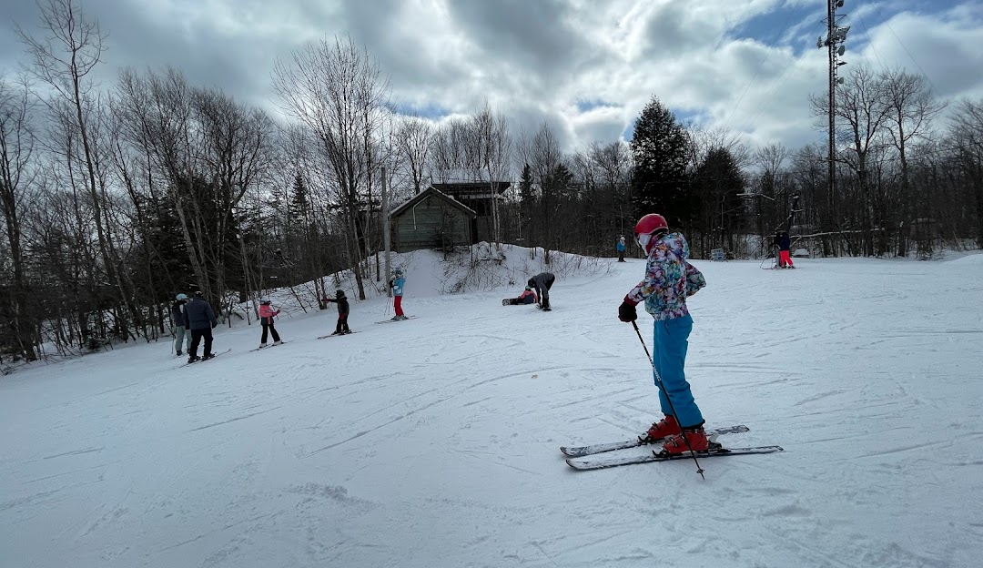 Winter sports scene at Montcalm in Lanaudière, Rawdon, Quebec, with a child learning to ski near a ski resort and chalet. A skier is also visible in the background.