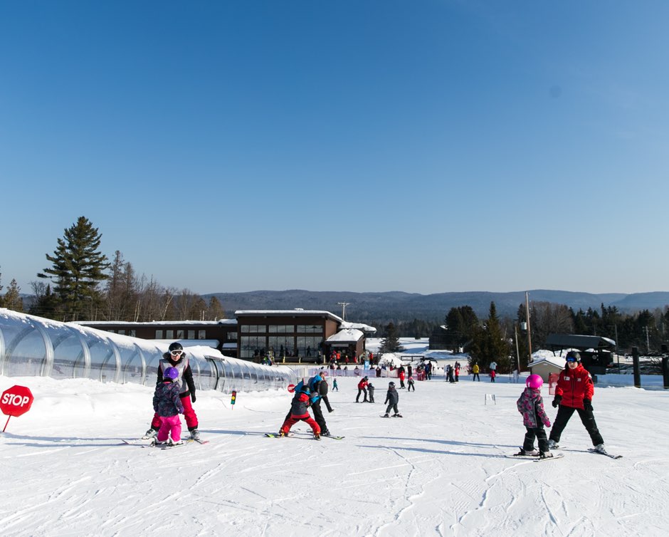 Winter sports enthusiasts enjoying a day of skiing at a resort in Montcalm, Lanaudière, Rawdon, Quebec. Every available slope is filled with skiers, ranging from groups to families. The scene perfectly encapsulates a bustling skiing hub.