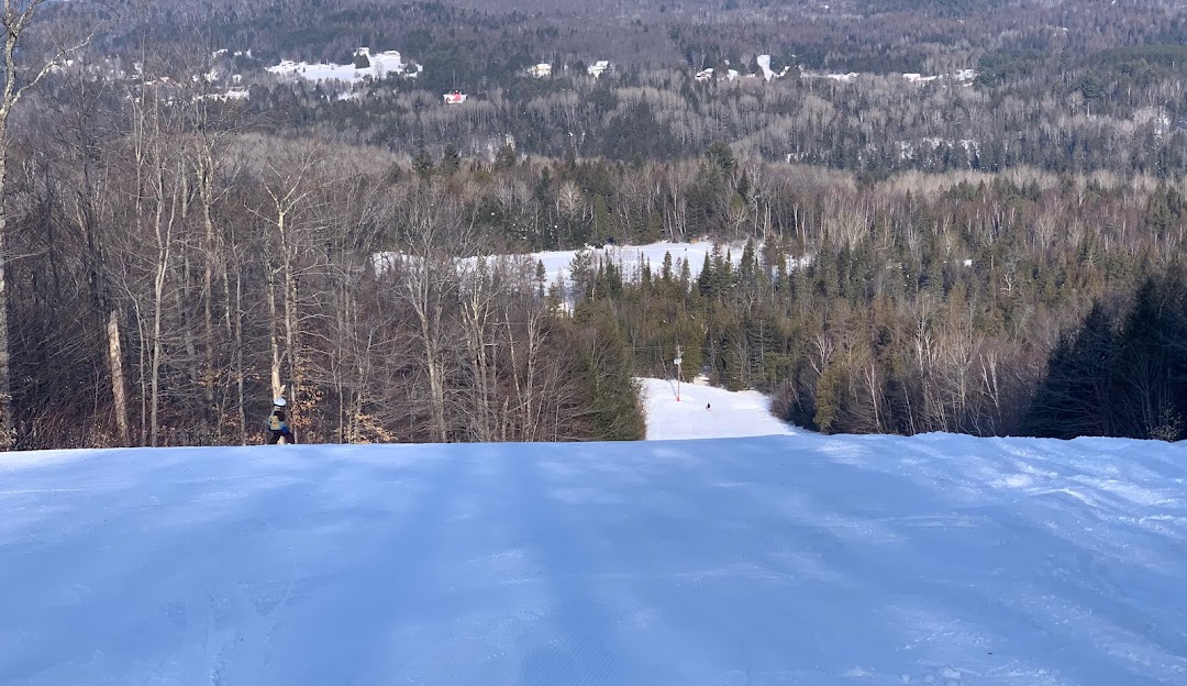 A skier glides down a snowy slope at the Montcalm ski resort in Rawdon Quebec. The winter sports scene is complete with a distant mountain backdrop and a nearby ski lift.