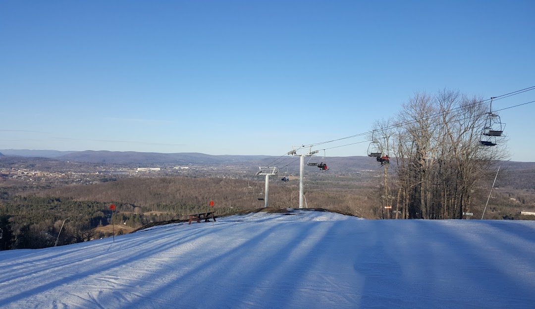 A winter sports scene at Bousquet ski resort in Pittsfield Massachusetts featuring a ski lift and a skier navigating snow-covered slopes.
