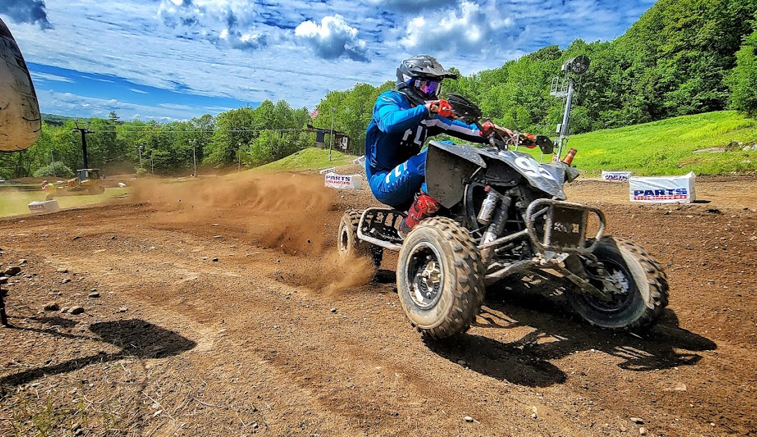 A snowmobile stands ready on Royal Mountain in Johnstown New York with a challet in the distance. Winter sports enthusiasts enjoy the snowy scene. A mountain bike suggests warmer adventures to come.