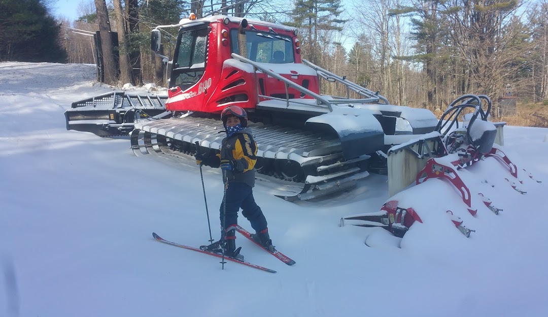 A skier and a snowmobile are spotted on Royal Mountain in Johnstown, New York. Surroundings encompass a winter sports scene with a chalet in the background, and a child learning to ski.