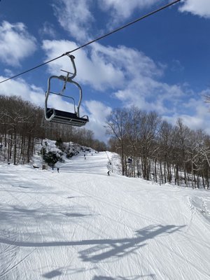 Ski lift ascending the snowy slopes of Big Bear at Masthope Mountain, Pennsylvania, with skiers enjoying winter sports and a challet visible in the background.