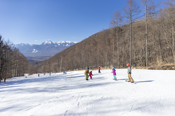Winter sports enthusiasts enjoying a day at Chateraise Ski Valley Nobeyama in Nagano, Japan. Skiers of all ages, including families, are present against a backdrop of snowy slopes and resort amenities.