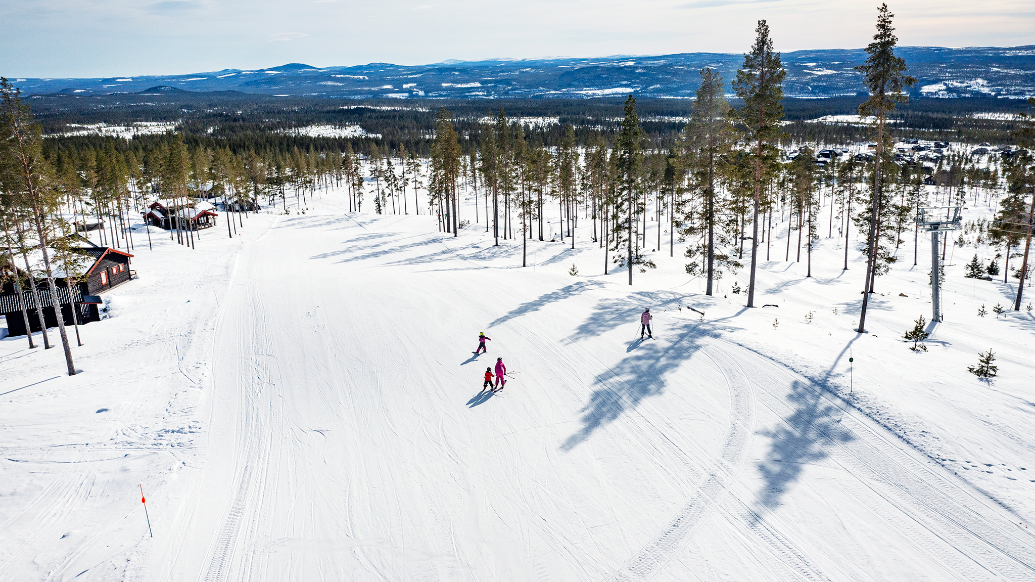 Winter sports scene at Idre Himmelfjäll, Sweden featuring a skier gliding down a snow-clad slope at a ski resort with a group of people skiing in the distance and a snowmobile nearby.