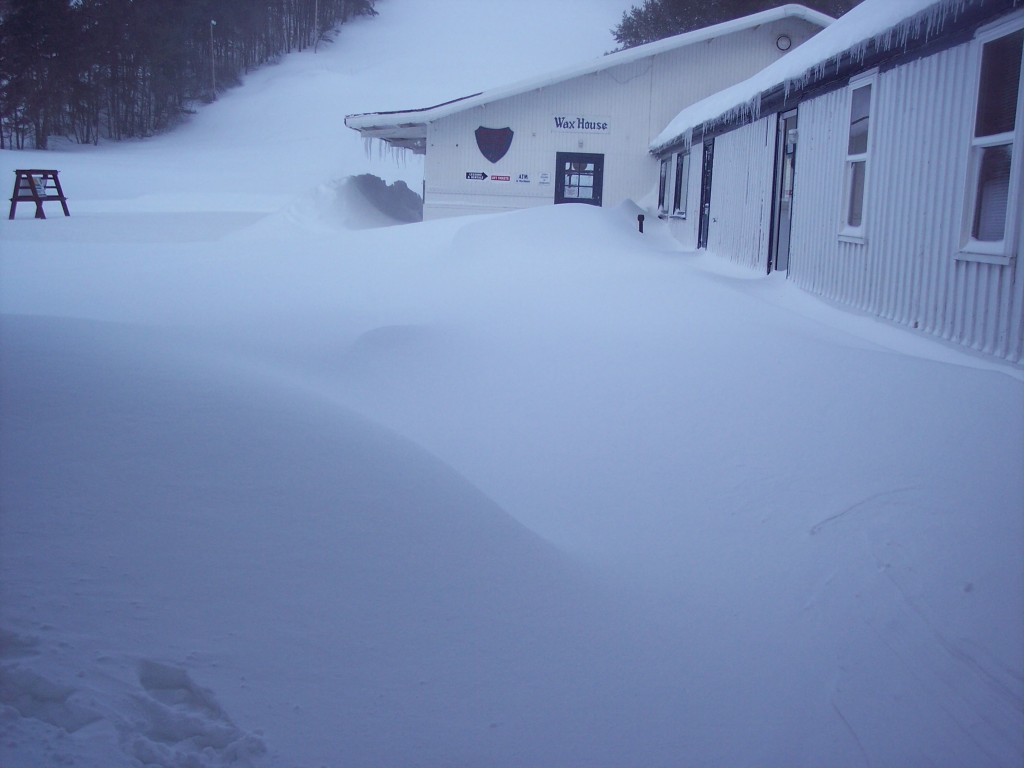 A vibrant winter sports scene at Snow Ridge The Adirondacks featuring an active ski resort with snowmobilers enjoying the snowy terrain nestled among cozy buildings.
