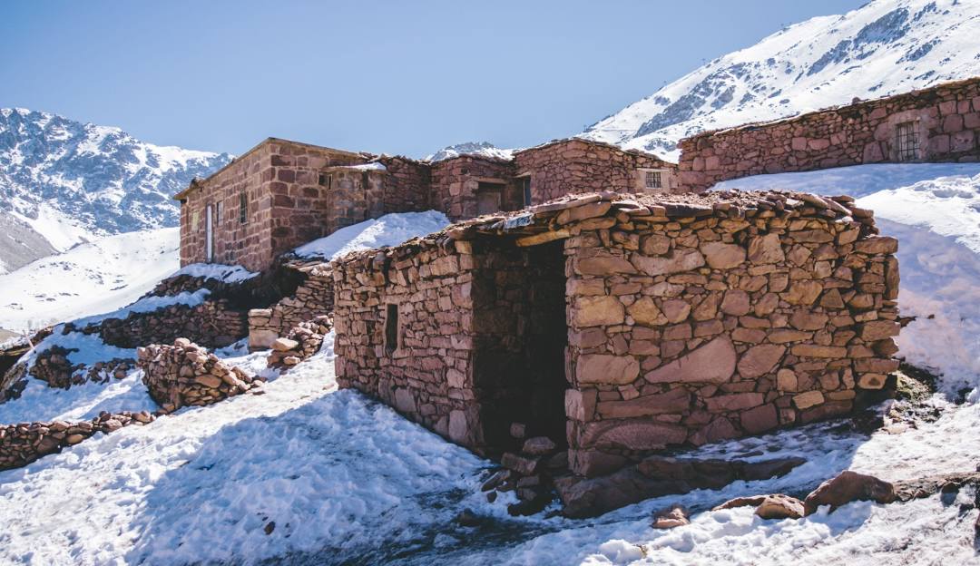 A picturesque chalet in the heart of Oukaïmeden, Morocco, surrounded by a mountainous winter sports scene. The focus of the image is a mountain hut doubling as a winter sports center.