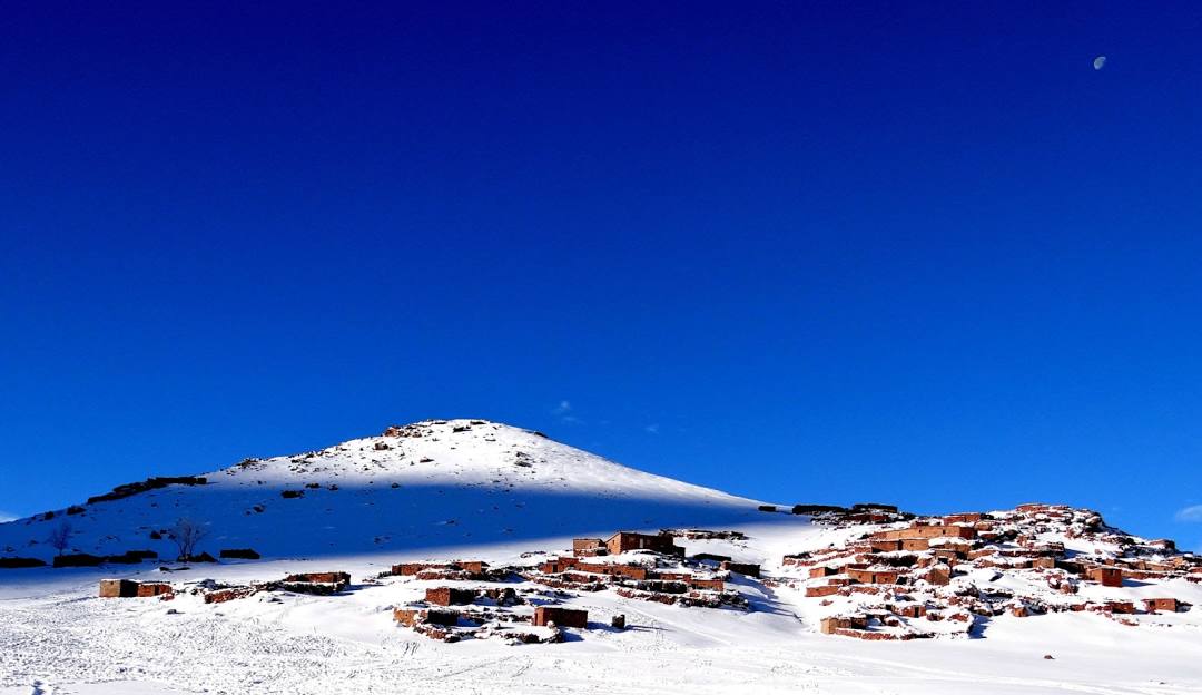 View of Oukaïmeden ski resort in Morocco, showcasing a chalet and mountain hut amidst the snow-covered mountains creating a vibrant scene of winter sports activities.