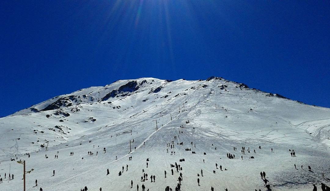 A picturesque view of Oukaïmeden in Morocco, featuring a charming chalet nestled amidst snowy terrain and mountains, with indication of a ski resort and skiers participating in winter sports.
