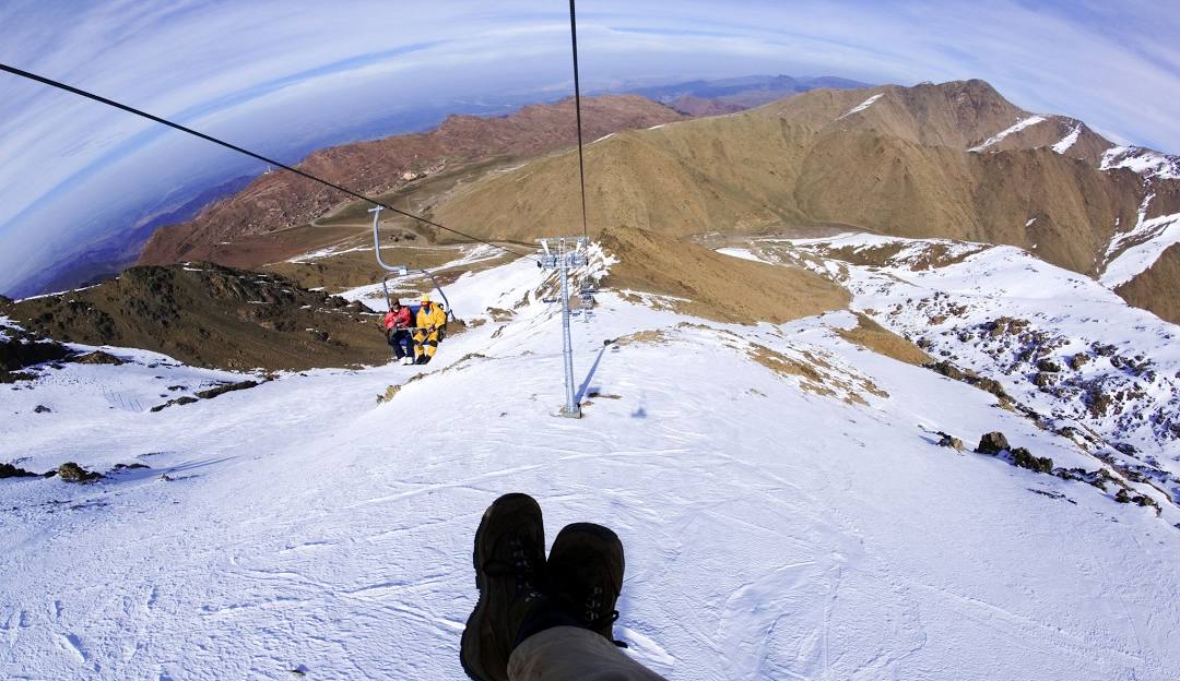A skier enjoying the slopes at Oukaïmeden ski resort in Morocco, with a ski lift and quaint chalet in the backdrop. A quintessential winter sports scene in full swing.