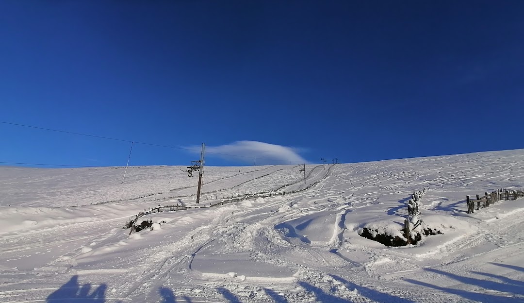 A skier on a snowy slope at Lecht Ski Centre, surrounded by the scenic Highlands mountain range. Nearby, a quaint chalet nestled in the tranquil Scottish resort stands as a warm contrast against the bustling winter sports scene.
