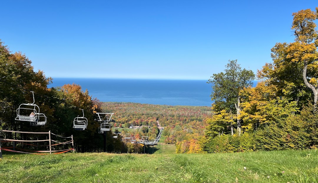 A scenic view of Porcupine Mountain in Michigan featuring a ski lift and ski resort amidst a winter sports scene. A chalet is also noticeable alongside a skier gliding down the slopes.