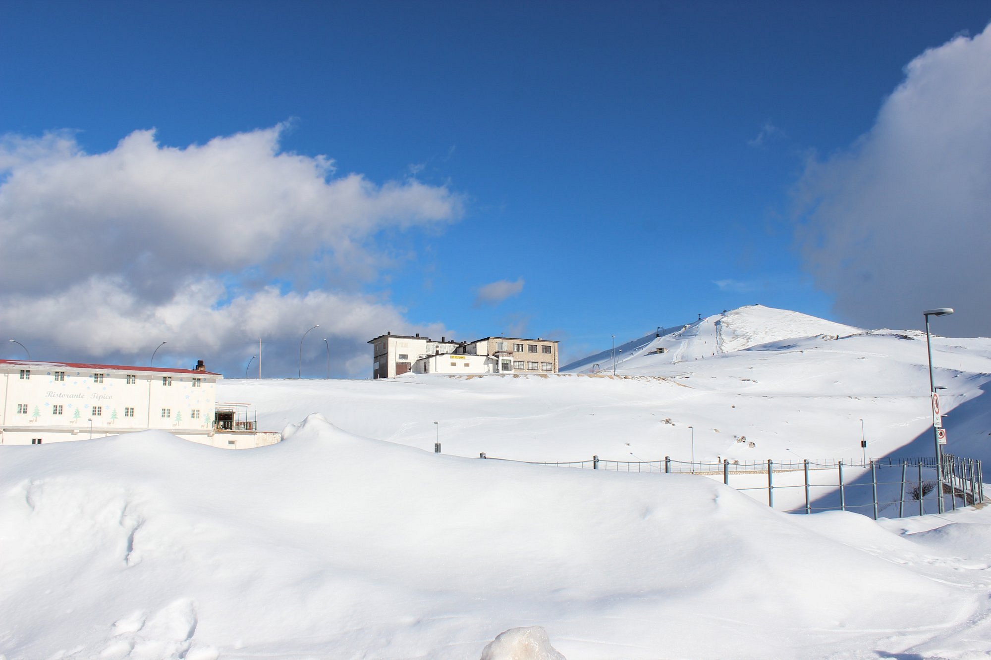 A winter scene at Campocatino, Frosinone, Italy featuring a chalet and a winter sports centre, surrounded by a stunning, snow-covered landscape.