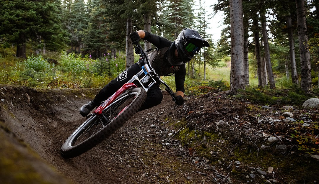 A mountain biker tackling a trail at Mount Sima in Whitehorse, Yukon, Canada, with a hint of a chalet in the distance.