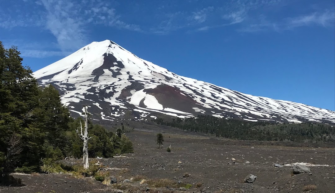 View of the majestic Volcán Llaima at Chile's Centro de Ski Araucarias with a hint of snow gracing the mountainside a quaint chalet and gears of a mountain bike visible.
