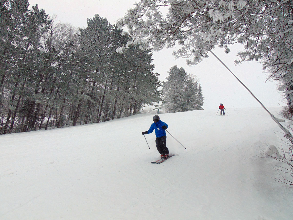 Winter scene at Mont Avalanche, Quebec, showcasing a skier in motion, a charming challet and the ski lift in the distance. The entire scene encapsulates the excitement of winter sports.
