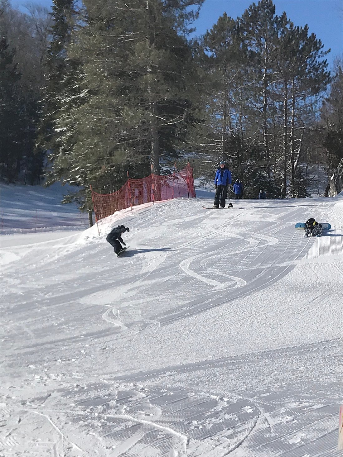 Winter scene at Mont Avalanche in Quebec, Canada featuring a skier gliding down the snowy slope. A group of people, perhaps a family, are also seen partaking in the winter sports activities at the ski resort.