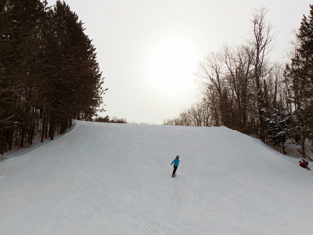A winter scene at Mont Avalanche, Quebec, featuring a skier navigating the snow-powdered slopes of the ski resort, with a chalet visible in the distance.
