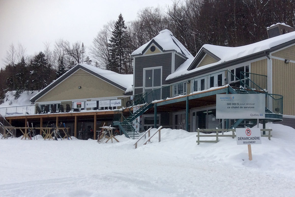 Winter scene at Mont Avalanche ski resort in Quebec, Canada featuring a bustling winter sports centre and a picturesque chalet surrounded by snowy slopes.