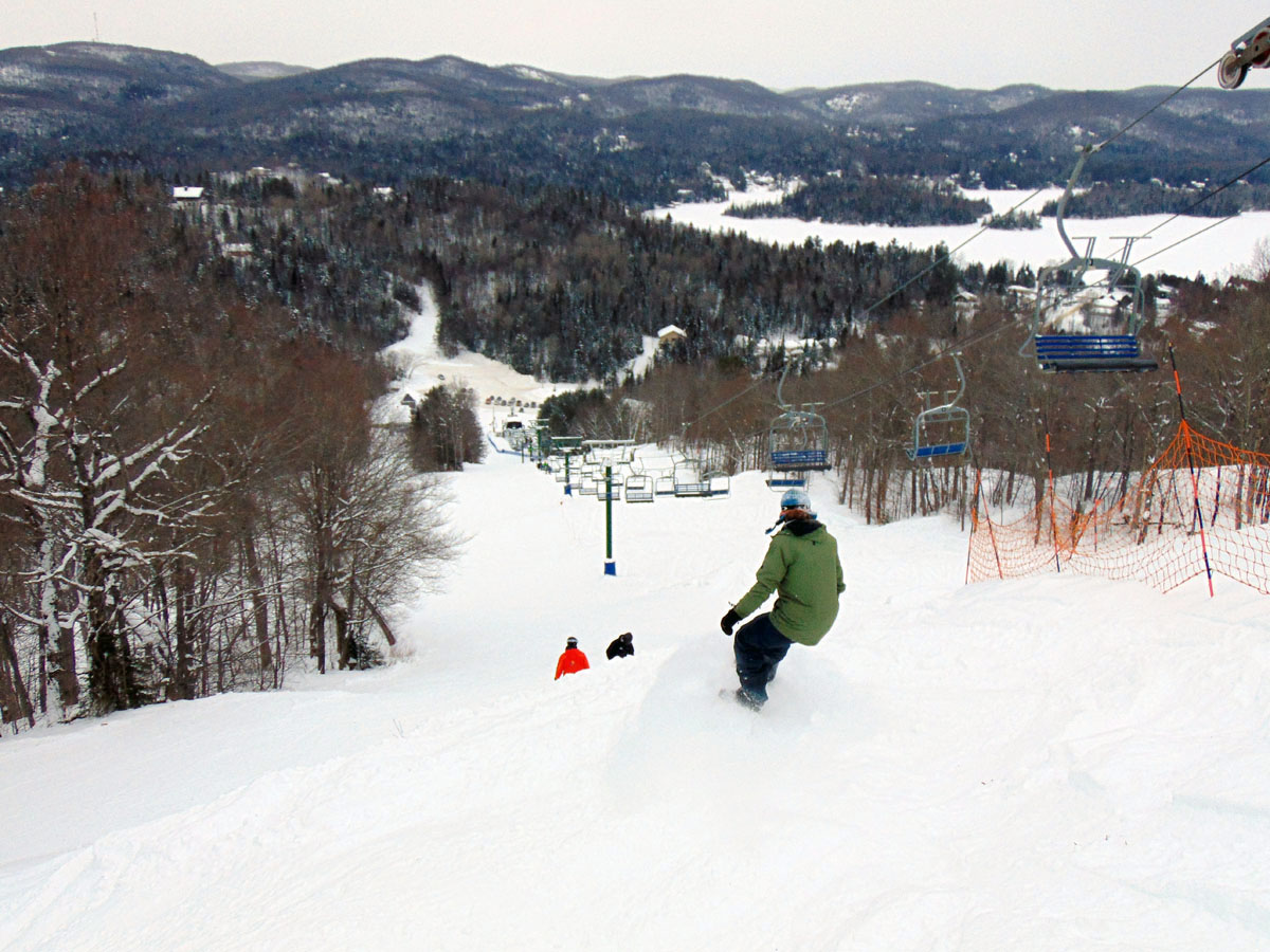 Winter sports scene at Mont Avalanche, Quebec, showcasing a ski resort with a ski lift, skier in action, and the bustling winter sports centre.