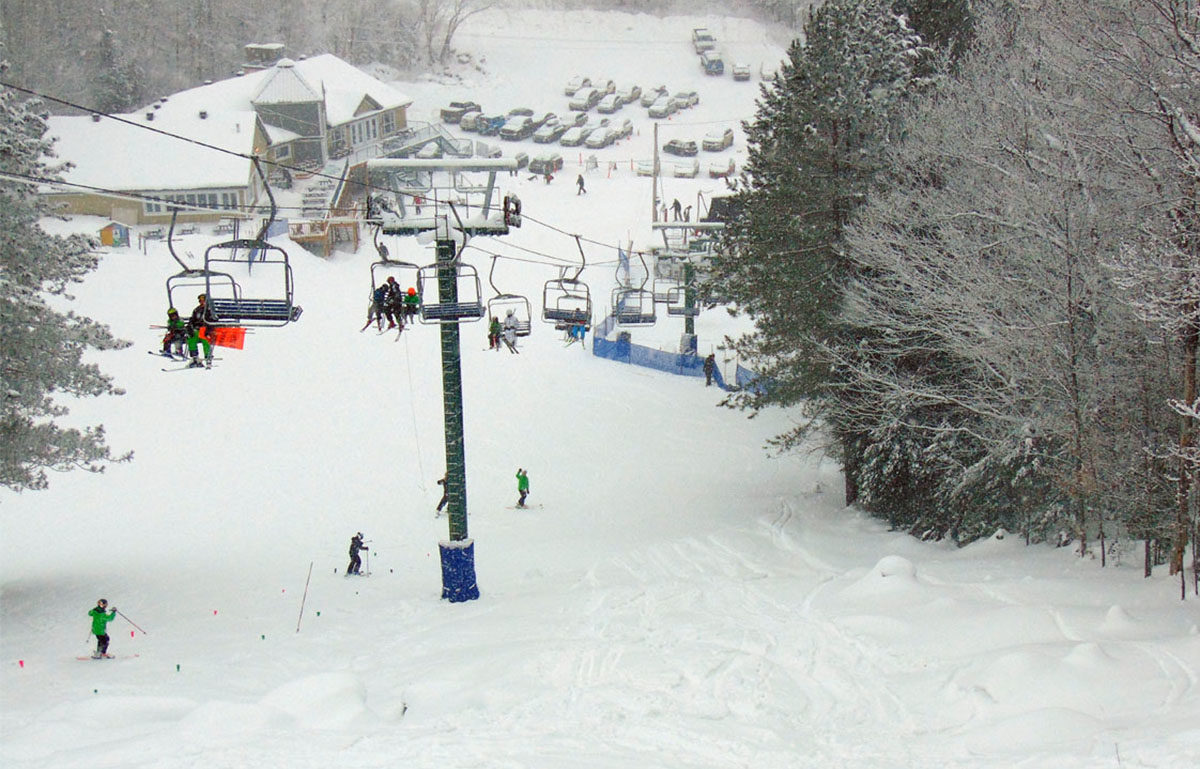 Bustling winter scene at Mont Avalanche in Quebec, Canada, featuring a ski resort with a visible ski lift and a skier performing winter sports.