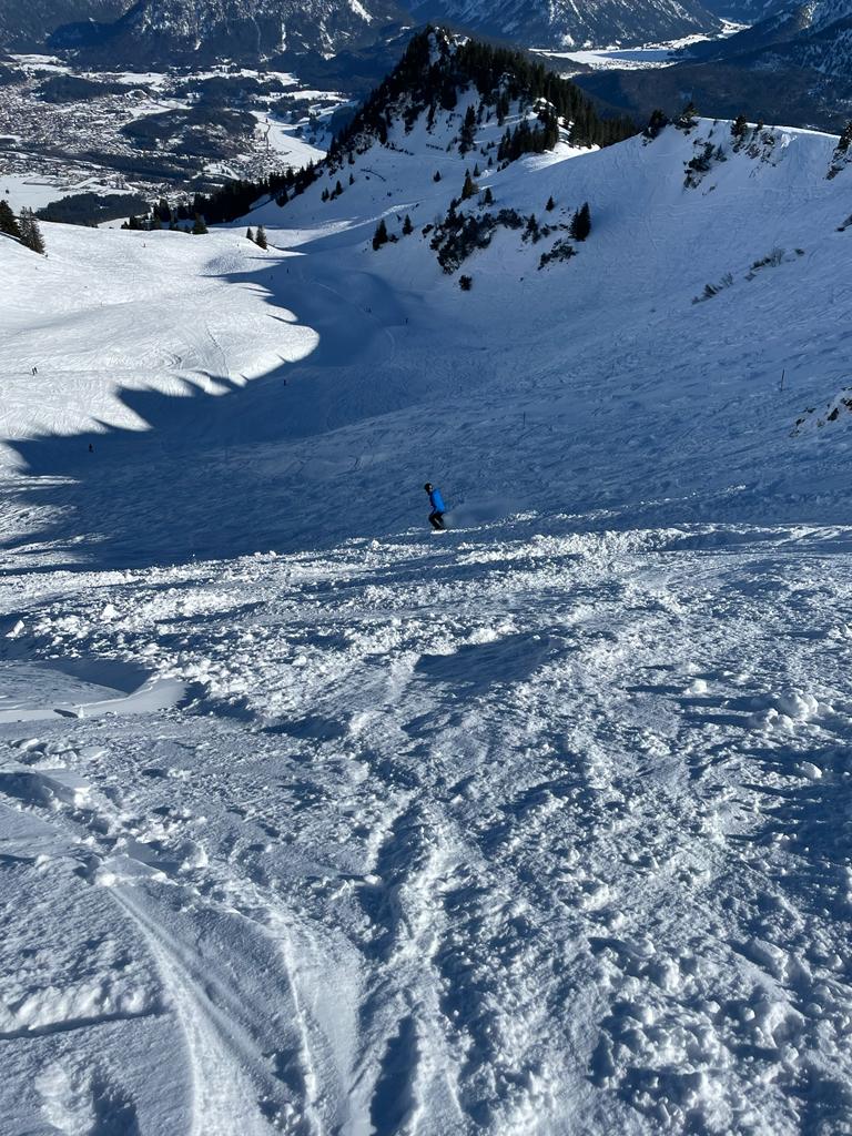 A skier making their way down the powdery slope at Breitenberg - Hochalpe - Pfronten ski resort in Germany, with a charming chalet and ski lift set against a snowy landscape.